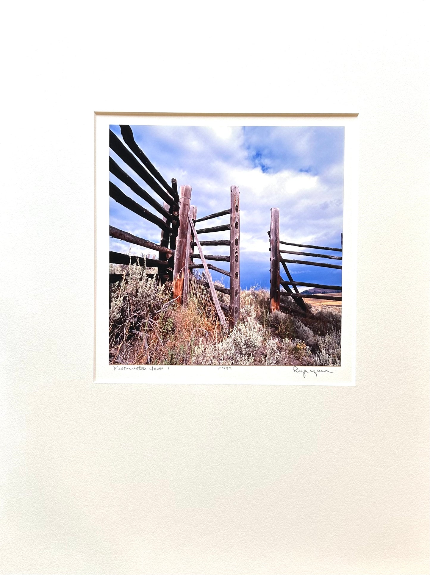 This photograph was taken in Yellowstone National Park on a Fall day. The fence with the open gate are old wood with uneven edges as in split-rail. The open gate bids you enter but the tall grasses are dry and are evident of lack of use. Through the gate the sky is soft with puffy clouds moving in a sea of cool blue.