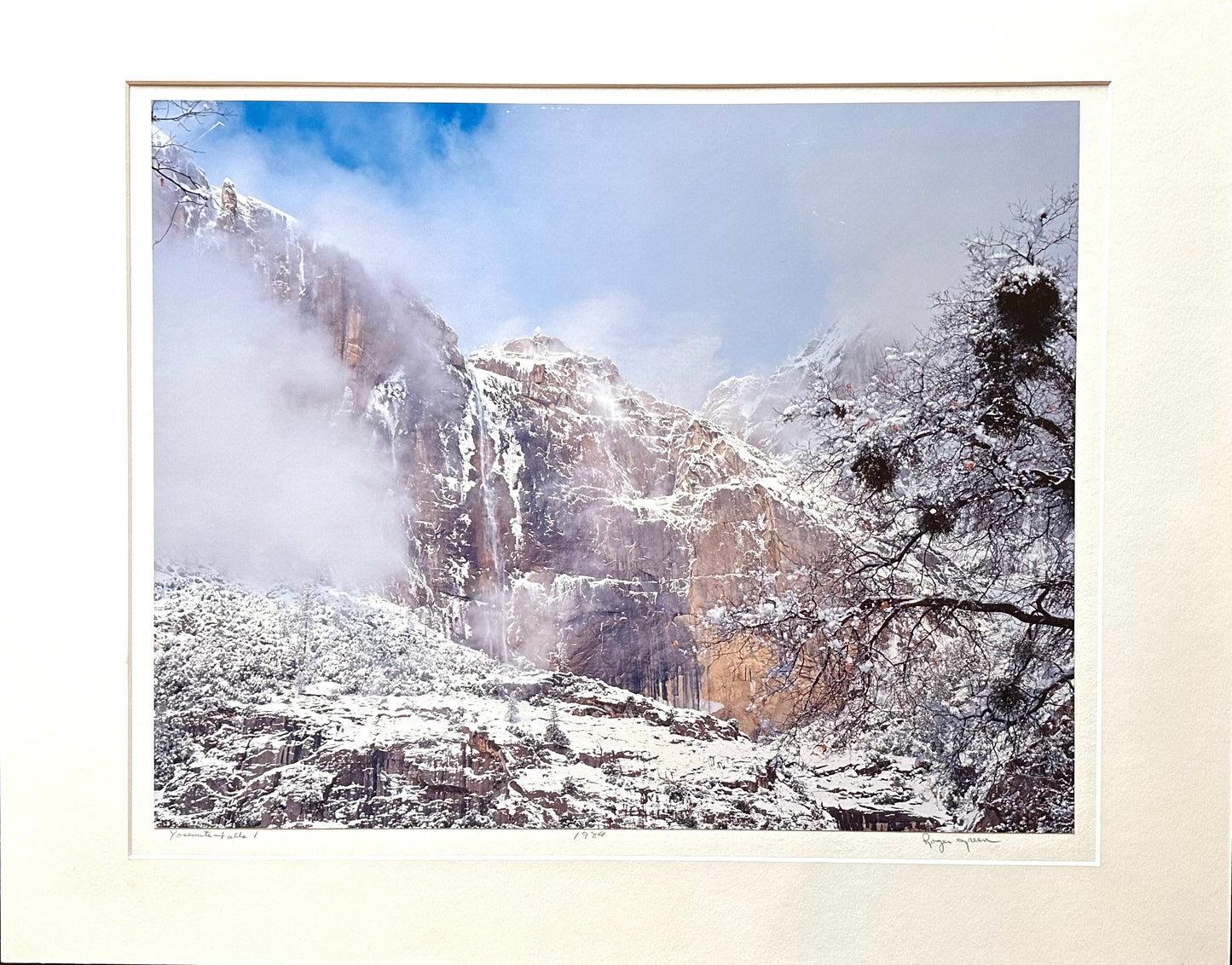 This photograph was taken in Yosemite National Park in the winter.The mountain was large and this is taken of the upper part only.  The foggy look of the clouds surrounded the upper portion of the rocks shrouded but still visible.  The rocks had a cascade of varnish coming down the front created by minerals.  A hint of the sky in the background is just barely visible in the coming fog. Trees look small in the foreground of the image, but only because the mountain is so large and magnificent.